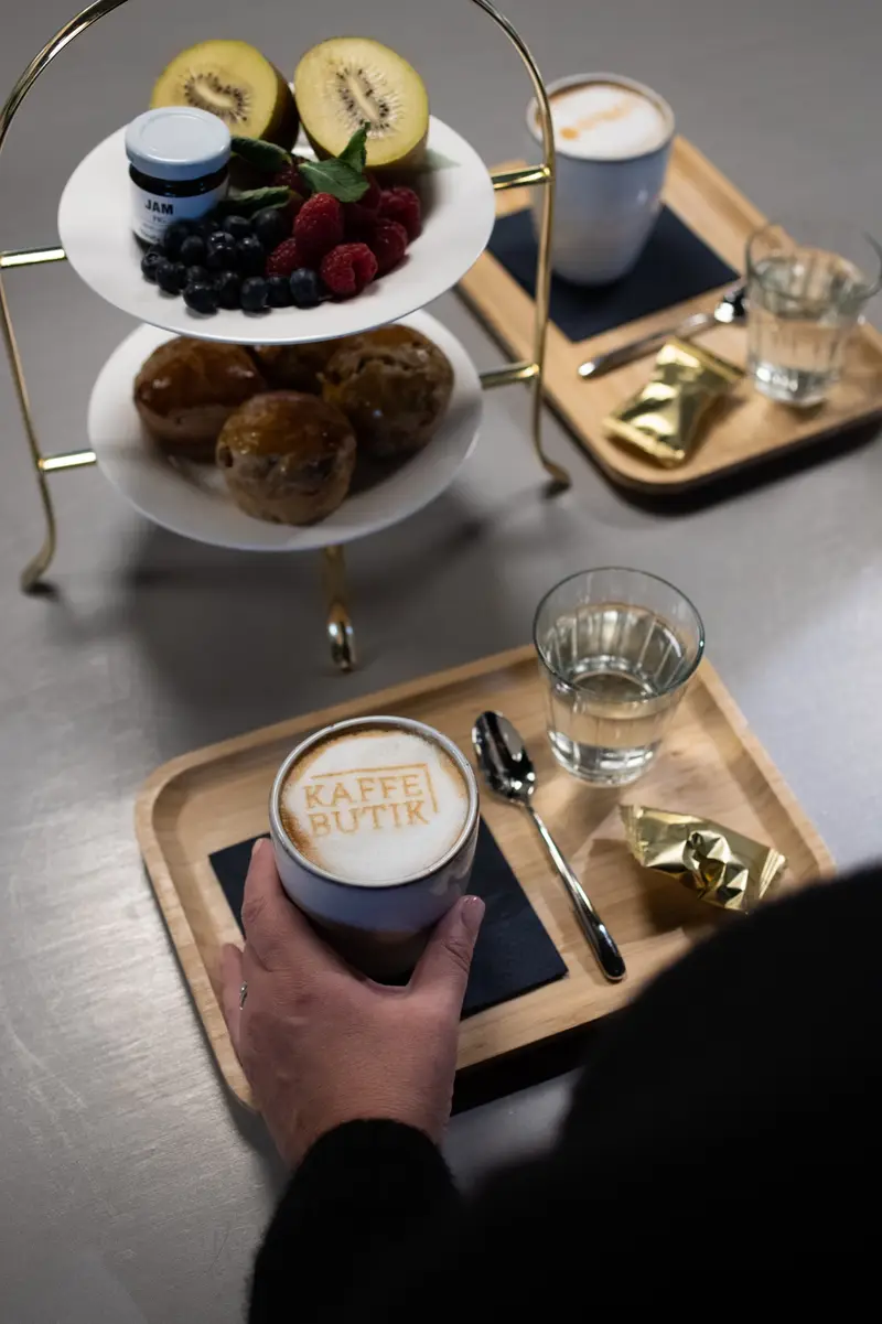 Etagere mit Früchten und Muffins, daneben ein Latte mit Kaffebutik-Schaum